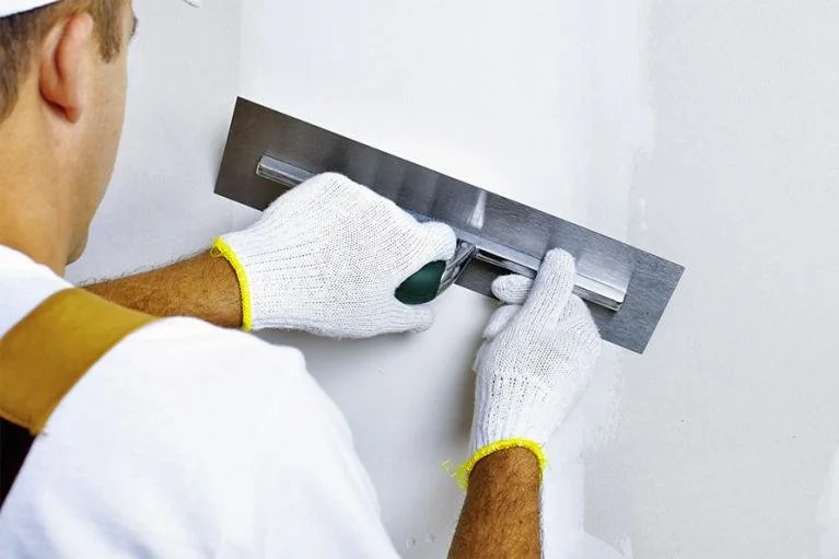 Un ouvrier pose une règle de maçon sur un mur pour faire une ligne de traçage.