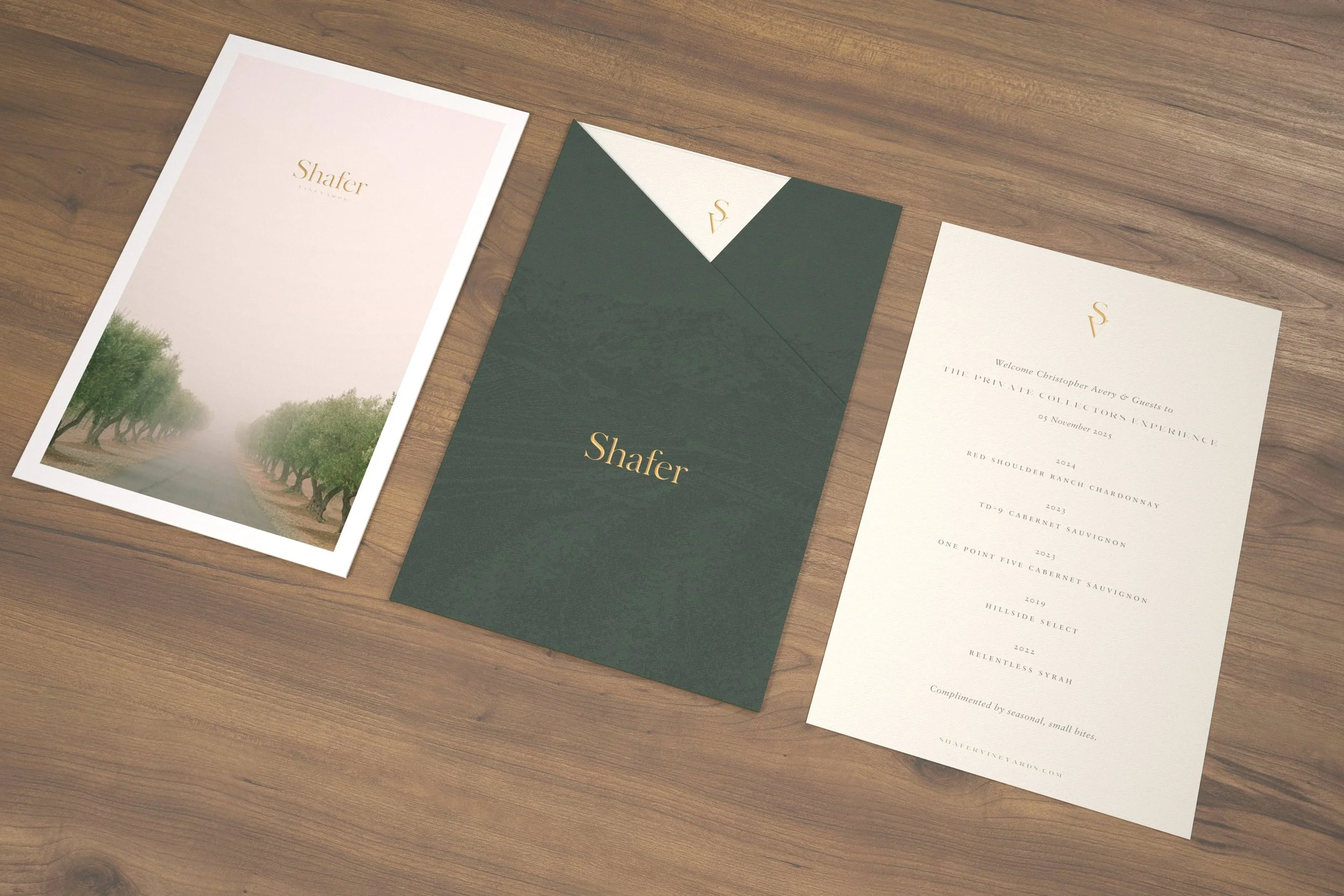 Wedding invitation suite with one main invitation, a folded green and white envelope with a gold logo, and a save-the-date card, all on a wooden surface.