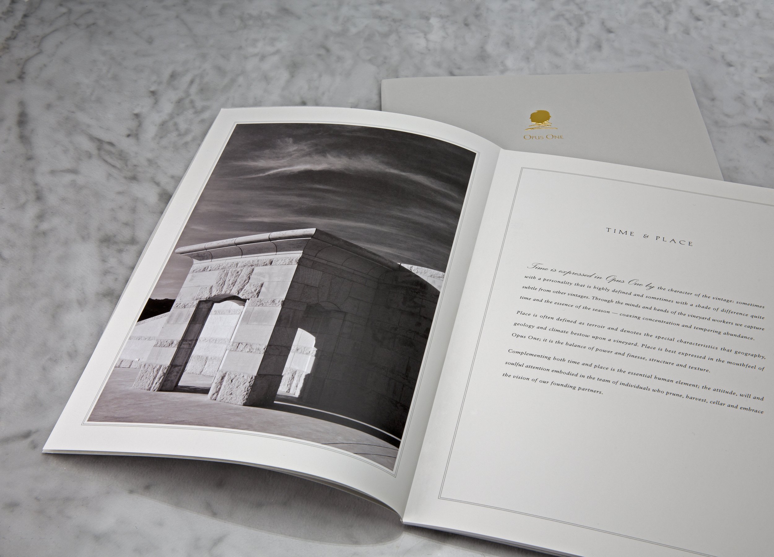 Open magazine with black and white photo of a modern building archway on the left page and text titled "Time & Place" on the right page, placed on a light gray textured surface.