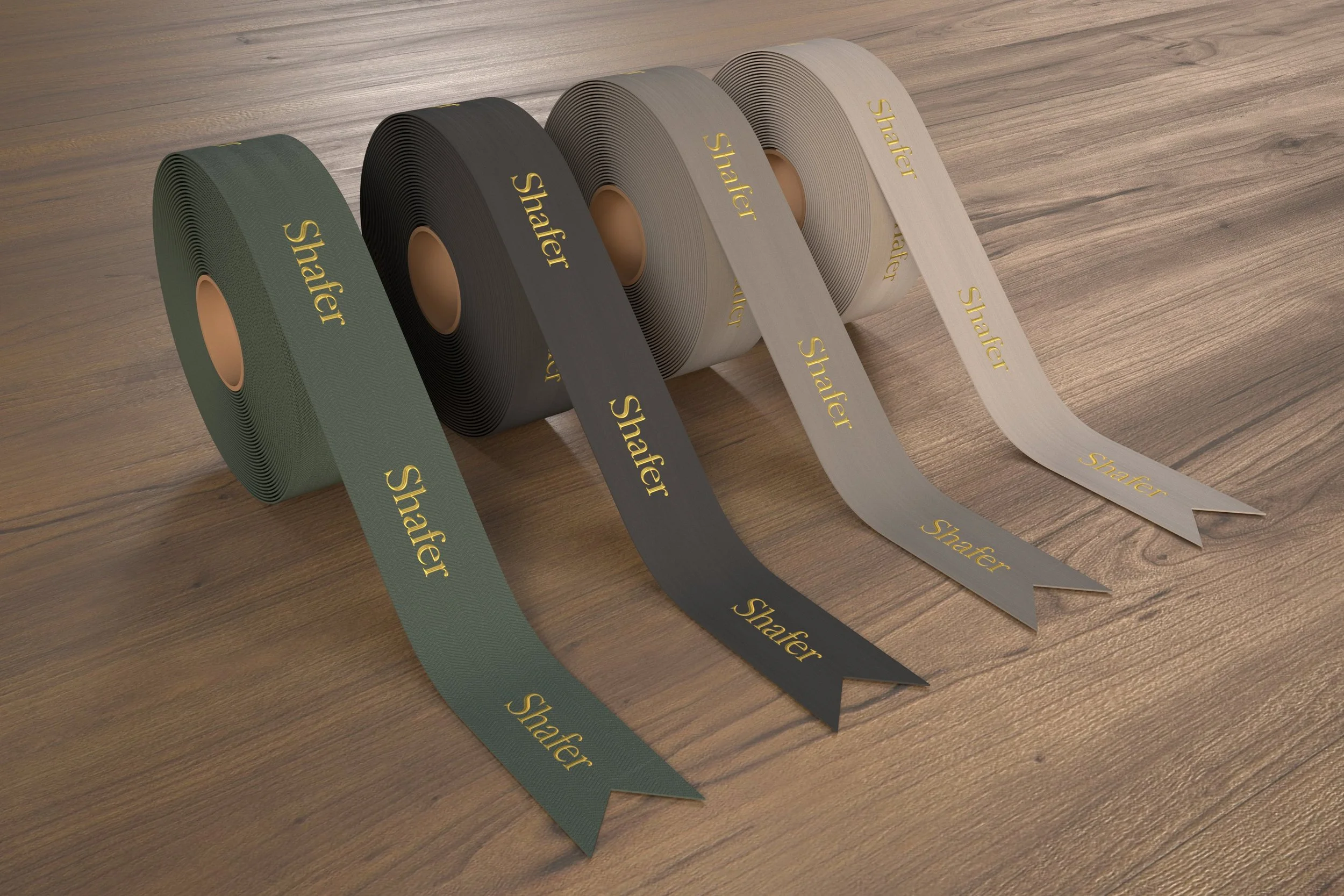 Four rolls of tape in green, black, gray, and white, each with the word 'Shafter' written in gold, laid out on a wooden surface.