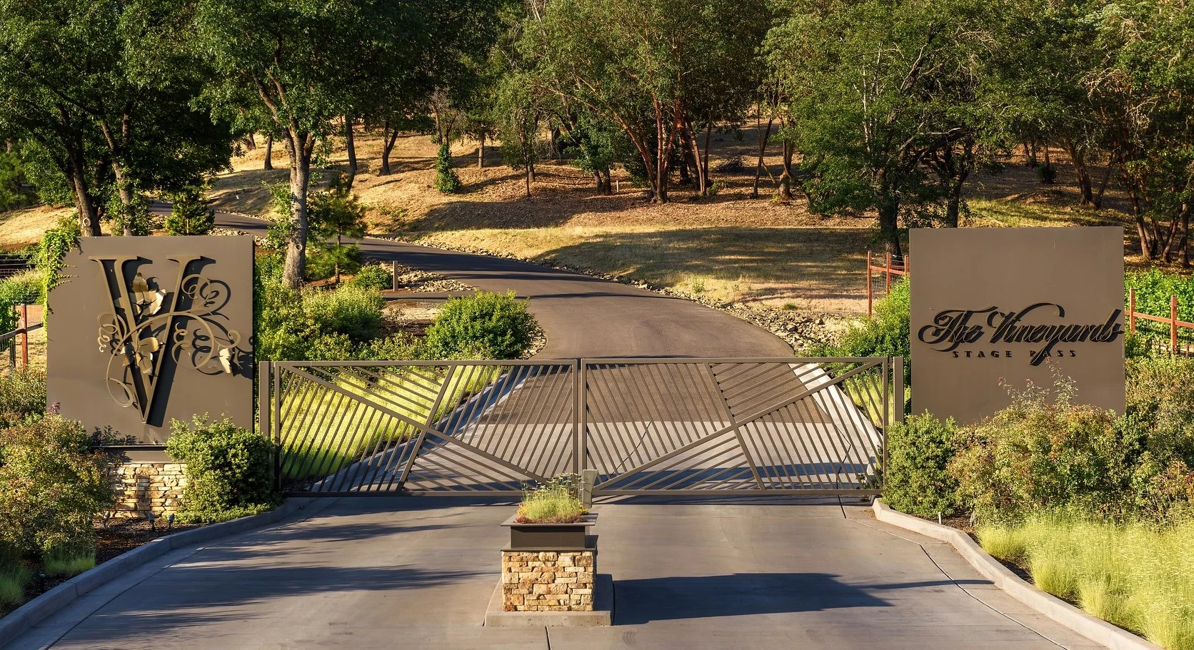 Gated entrance to The Vineyard stage pass with a decorative logo, surrounded by greenery and trees in the background.