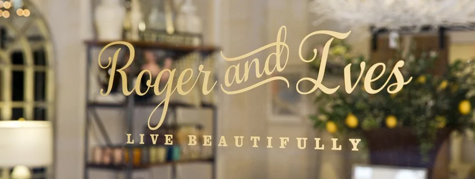 Decorative window with text 'Roger and Lves Live Beautifully' over a cozy, warmly lit interior with shelves and plants.