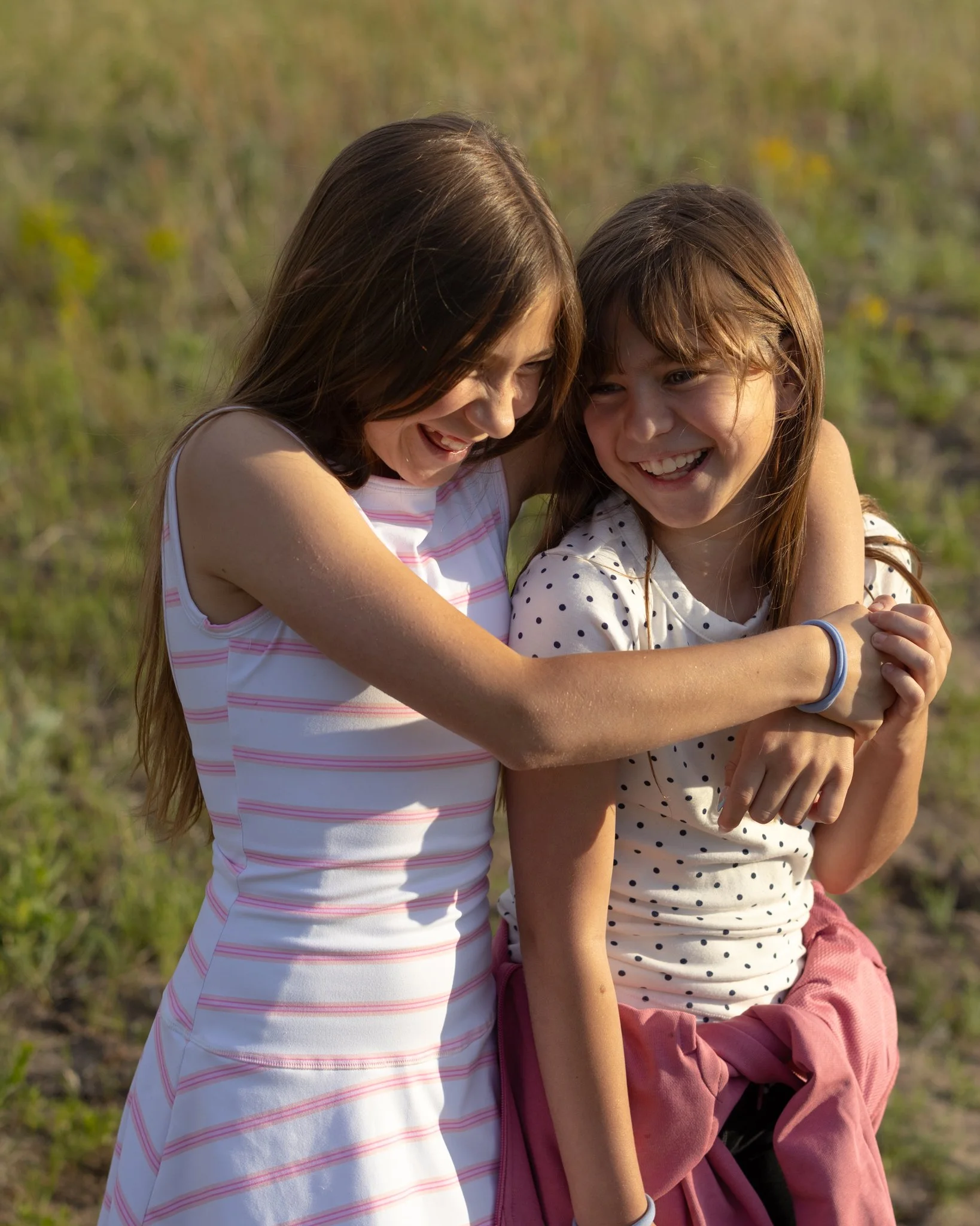 A candid portrait of two young girls smiling and laughing together outdoors, with a blurred natural background