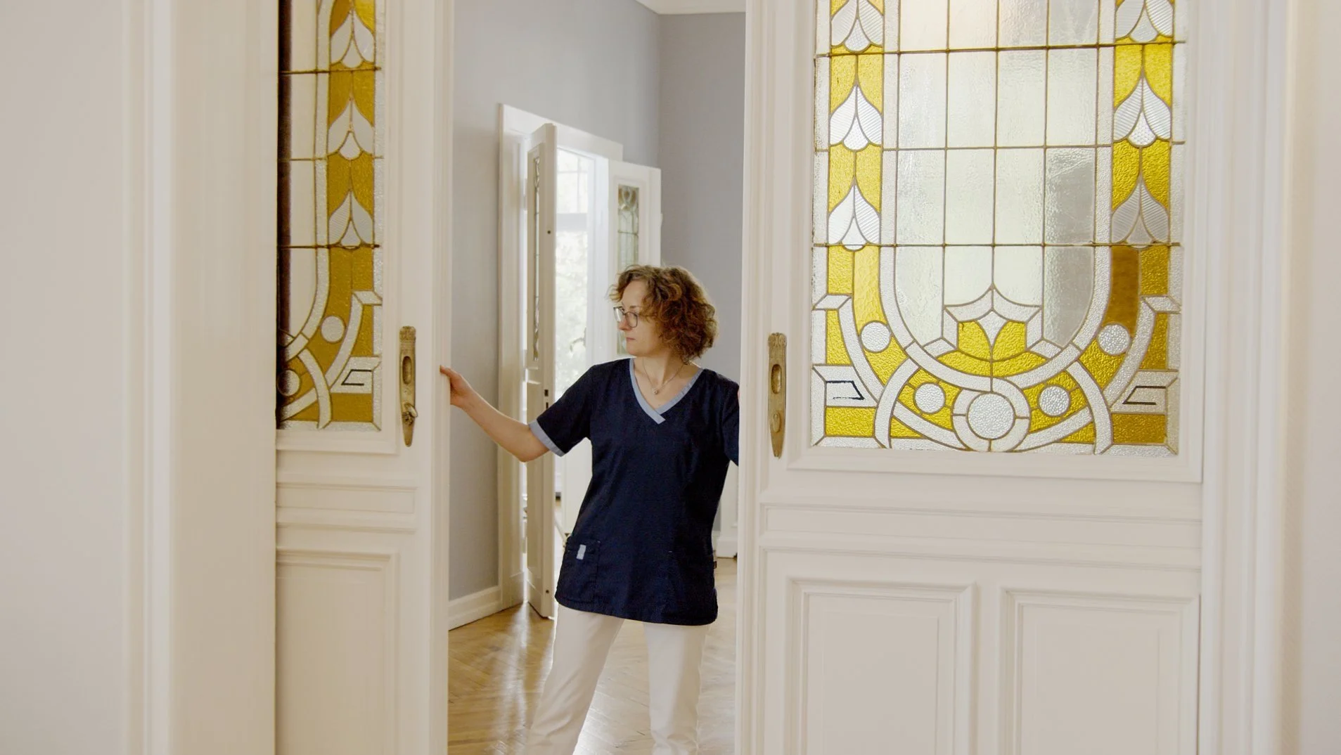 Frau öffnet eine große Tür mit buntem Glasfenster im Innenraum eines Hauses.