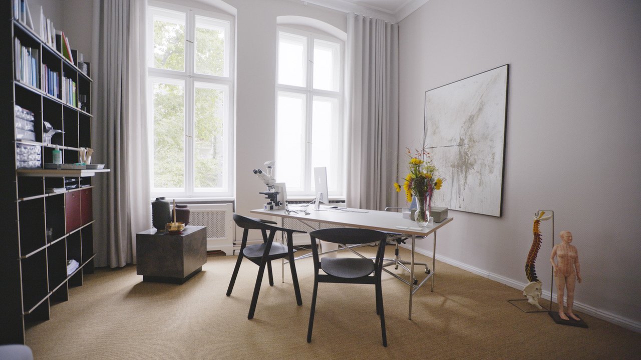 Ein modernes Arzt- oder Wissenschaftlerbüro mit Schreibtisch, Computer, Mikroskop, Bücherregal, Kunstwerke, Blumen und anatomische Modelle.