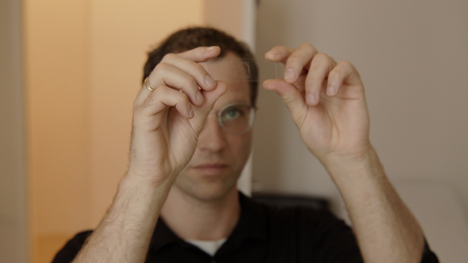 Mann mit Brille hält eine Linse vor das Auge.