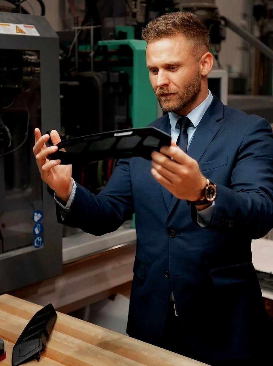 Un homme en costume regardant une tablette dans un atelier ou un environnement industriel.