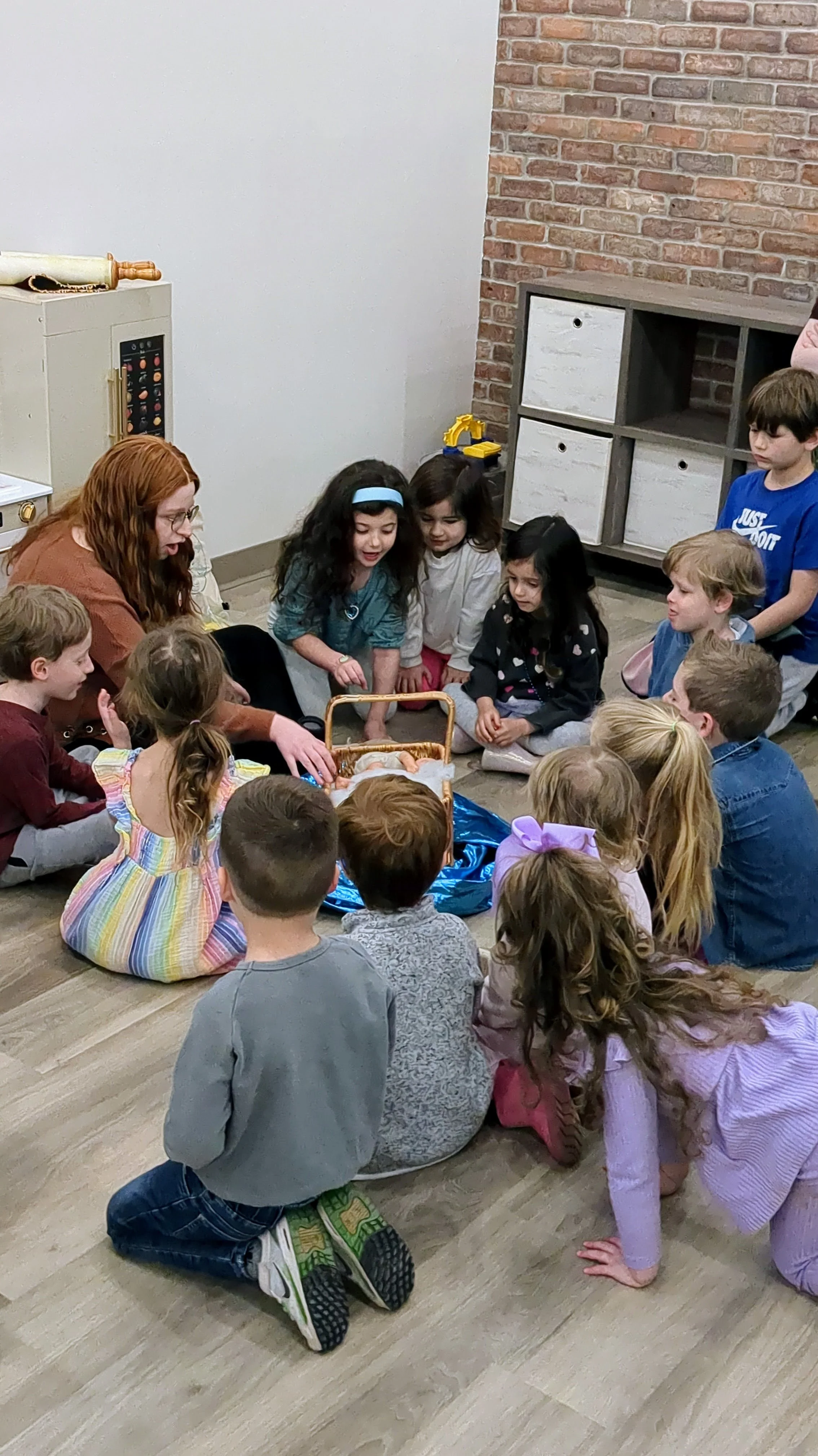 Children and an adult gathered around a small manger with a doll.