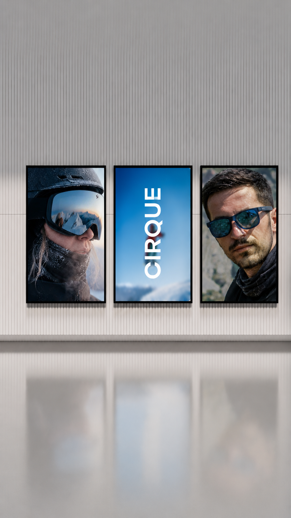 Three large posters on a wall. The middle poster has the word "CIRQUE" on a blue sky background. The left poster shows a person with snow and mountain scenery reflected in their ski goggles, wearing a helmet. The right poster features a man with shor
