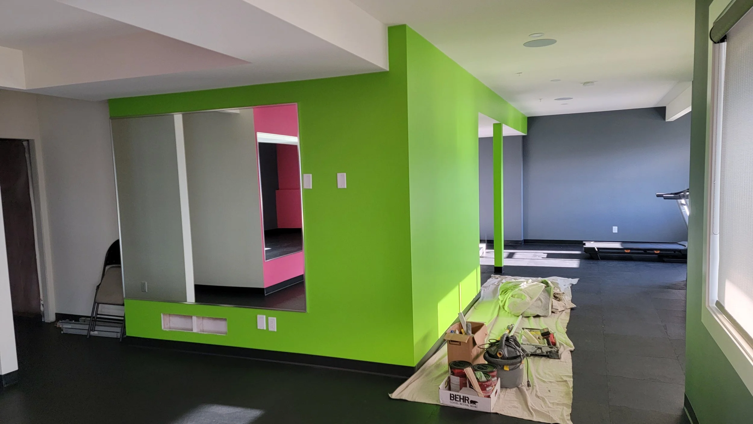 Room under construction with a green wall, a pink wall section, a large mirror, and construction tools and materials on the floor.