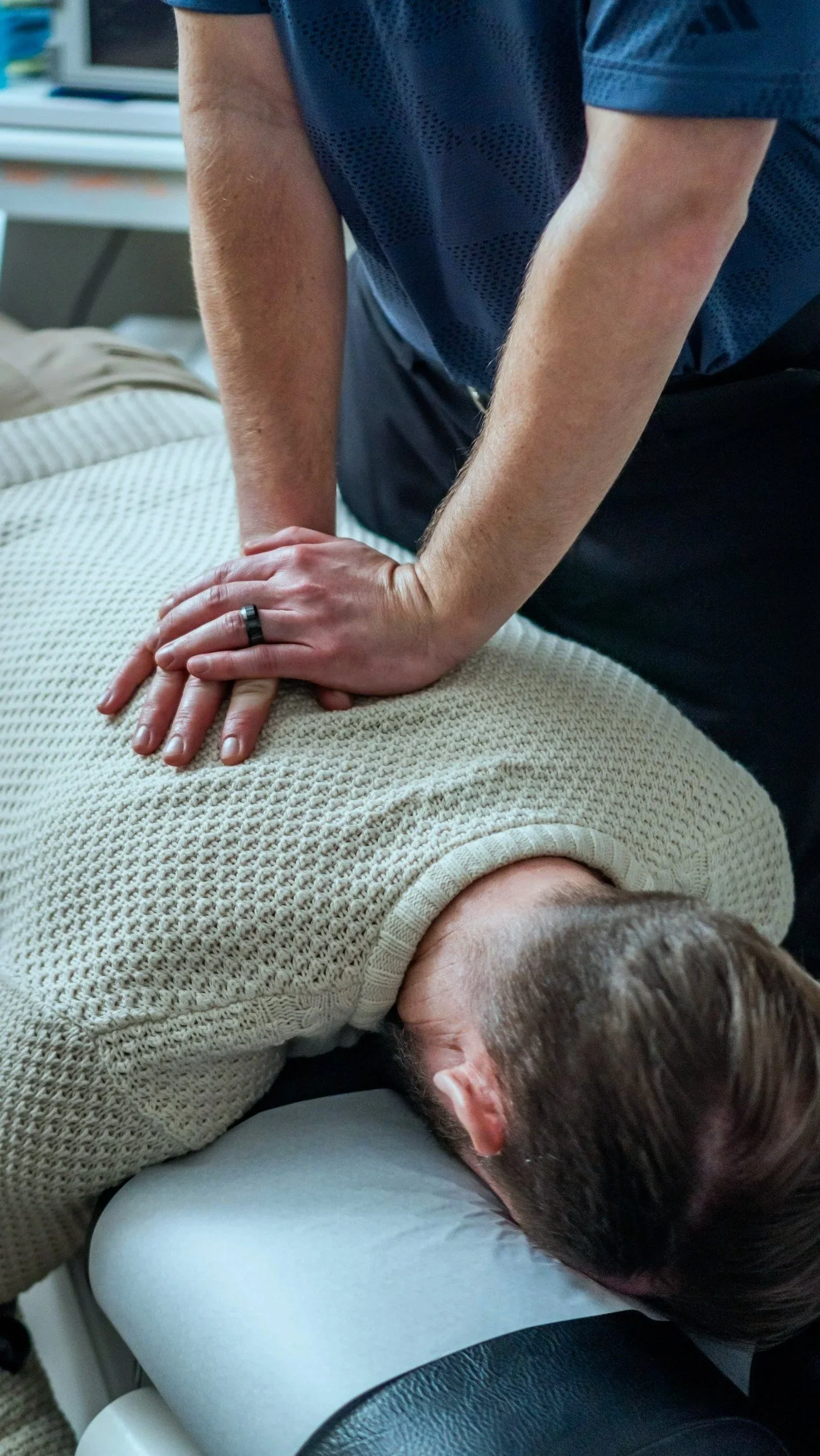 Person performing  chest compressions during a CPR training, covering the chest of a man lying on an examination table.