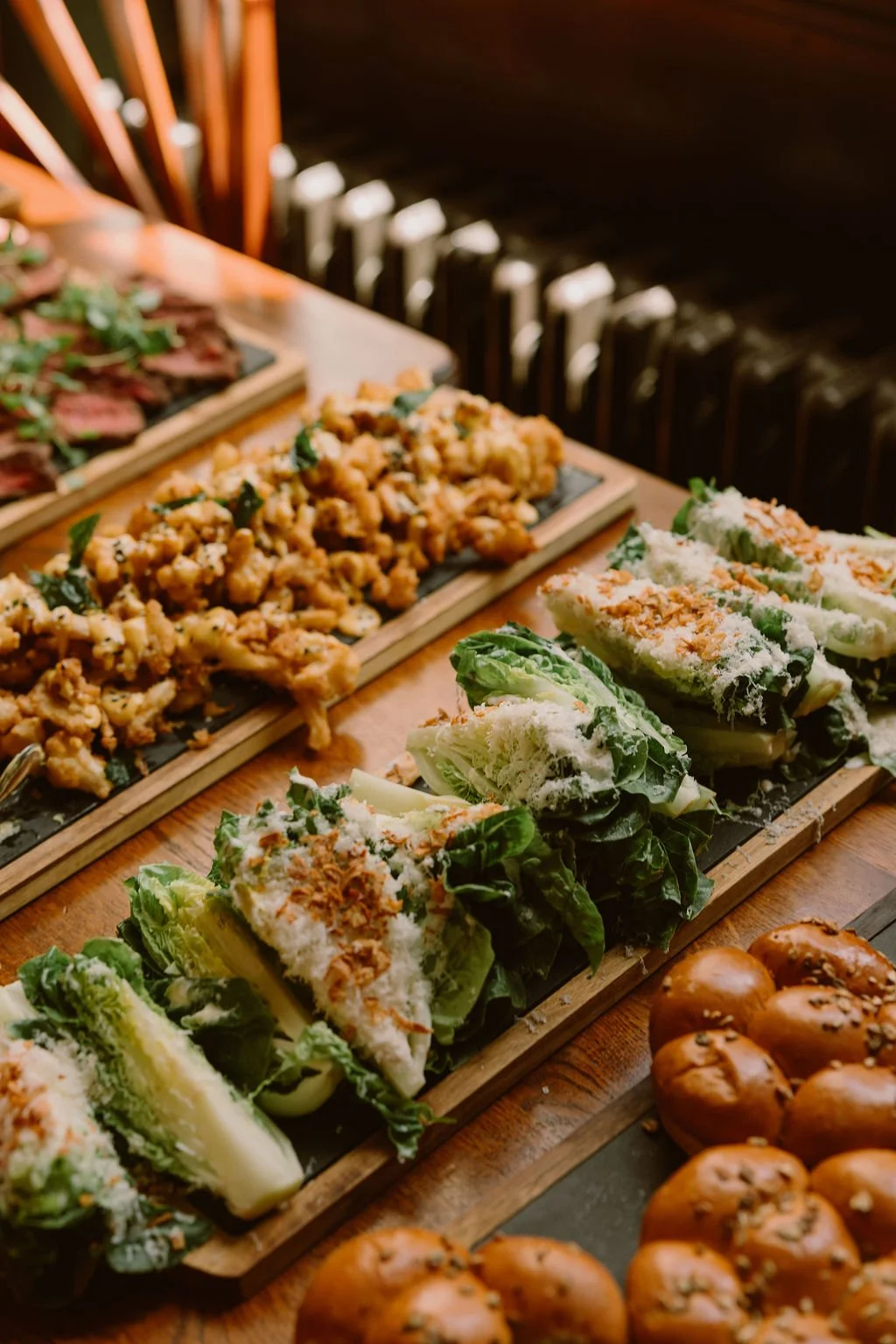Assorted Asian-inspired appetizers on black boards, including lettuce wraps with shredded chicken, fried chicken bites, and fried egg balls, on a wooden table.