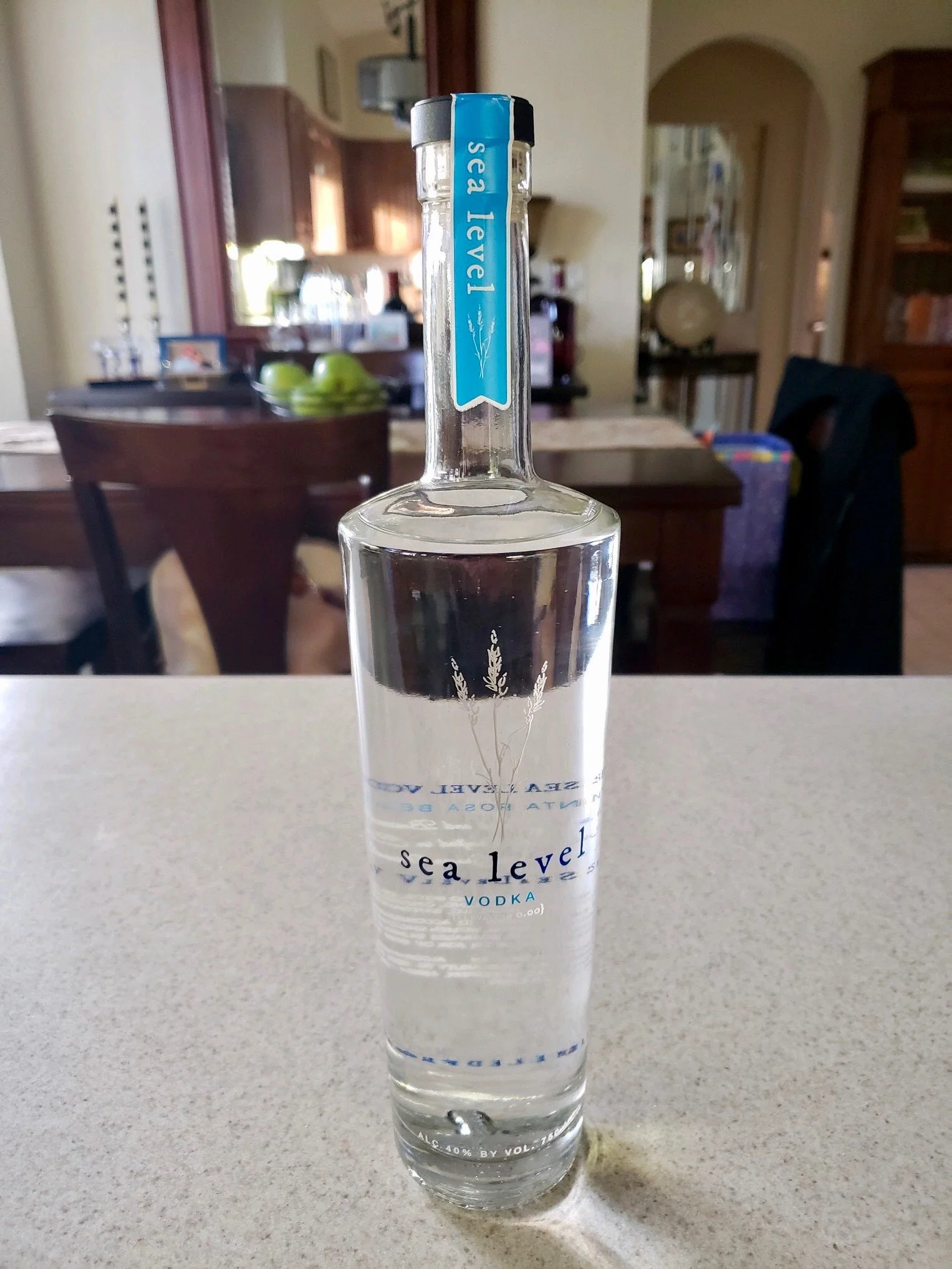 A tall, clear bottle of Sea Level vodka with a blue seal on the neck, placed on a light-colored countertop in a kitchen or dining area.