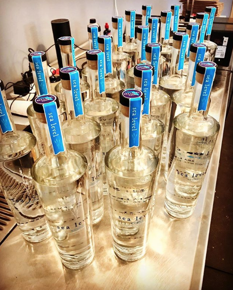 Multiple glass bottles of water with blue sea level labels, arranged on a table.