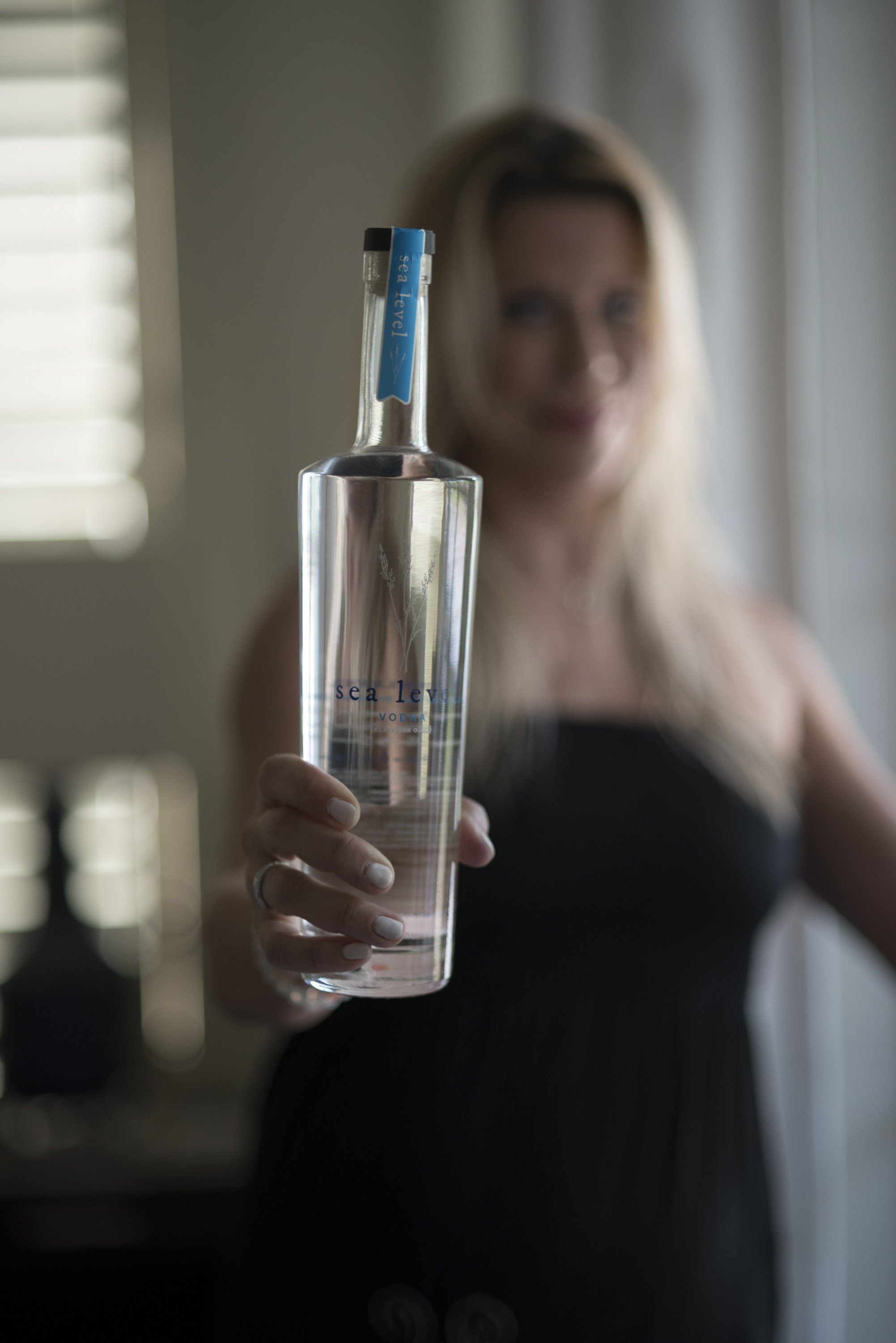 Woman holding a clear bottle of Sea Level vodka, with a blurred background.