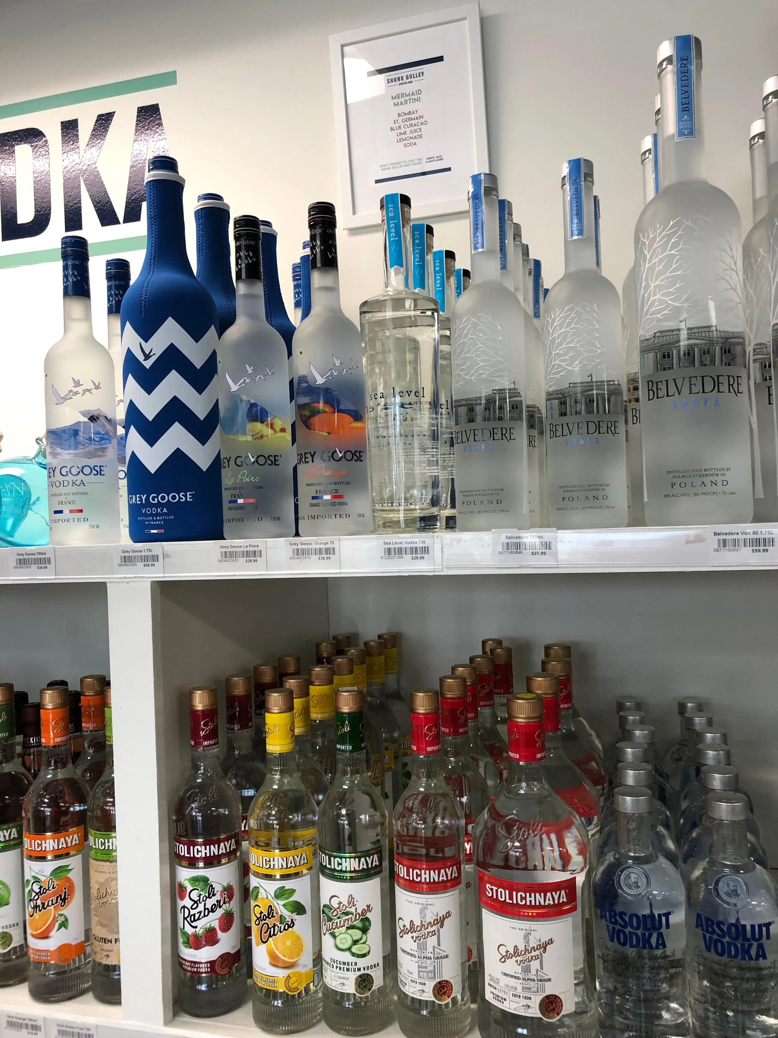 Display of various bottles of vodka on store shelves, including Grey Goose, Belvedere, Stolichnaya, and Absolut.