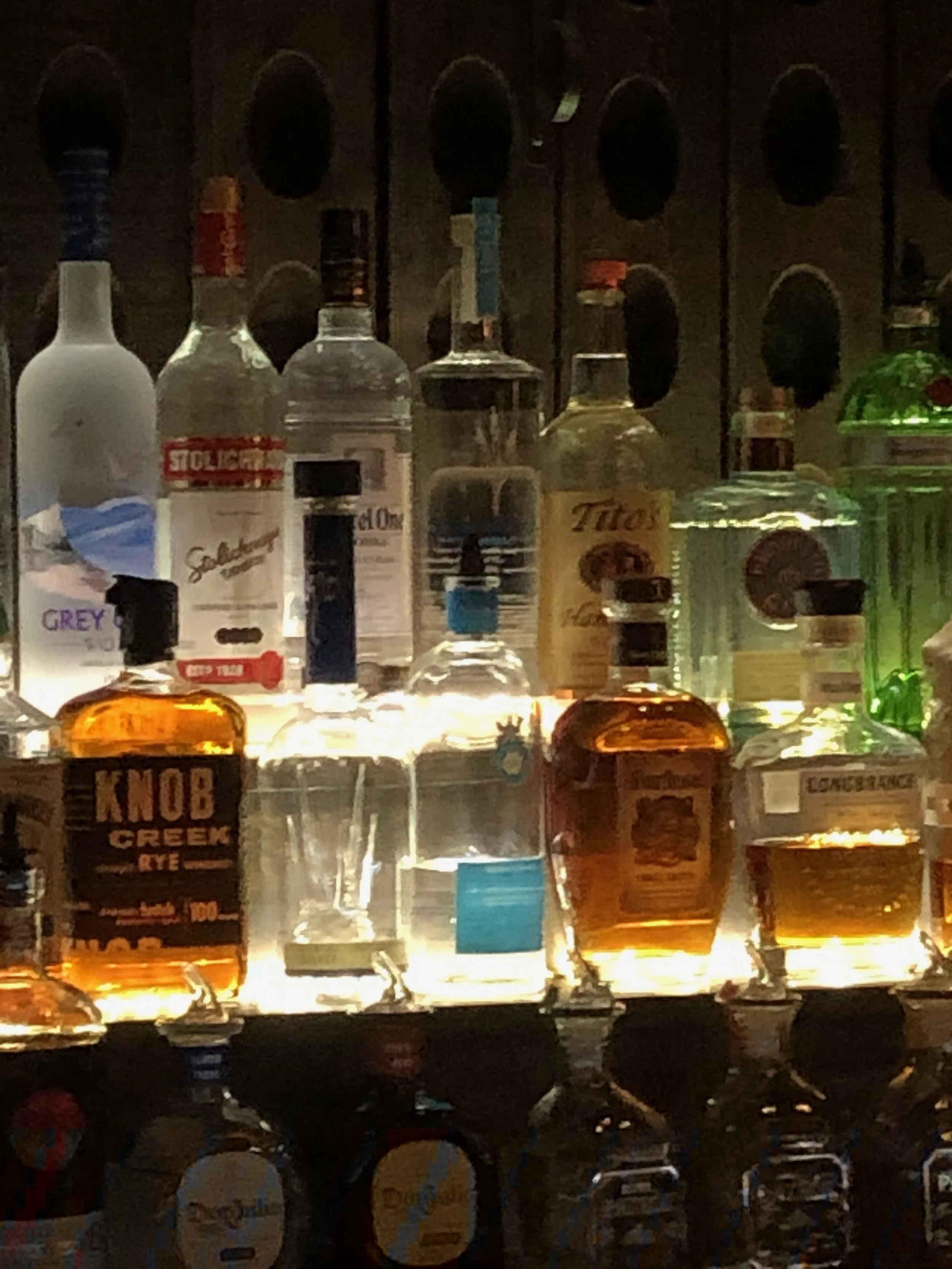 Backlit display of various liquor bottles on a bar shelf.