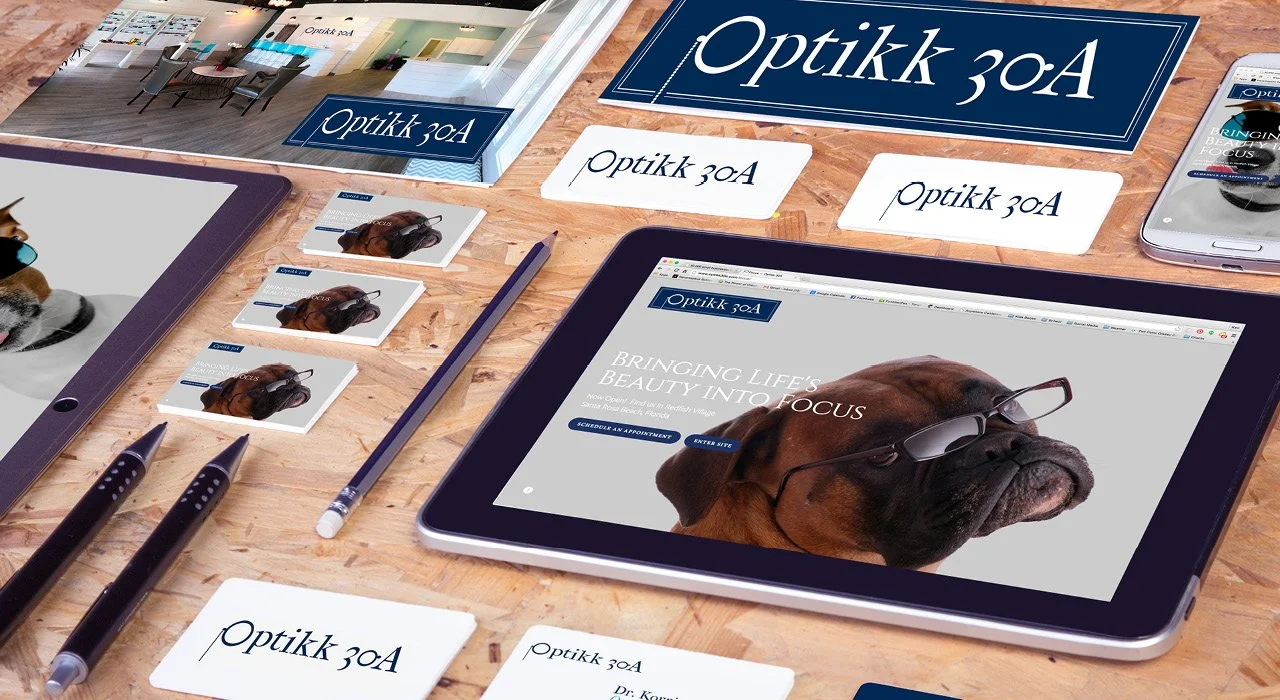 A desk displaying branding materials for an optometry business, including a website on a tablet, business cards, a sign, and promotional items featuring a dog wearing glasses.