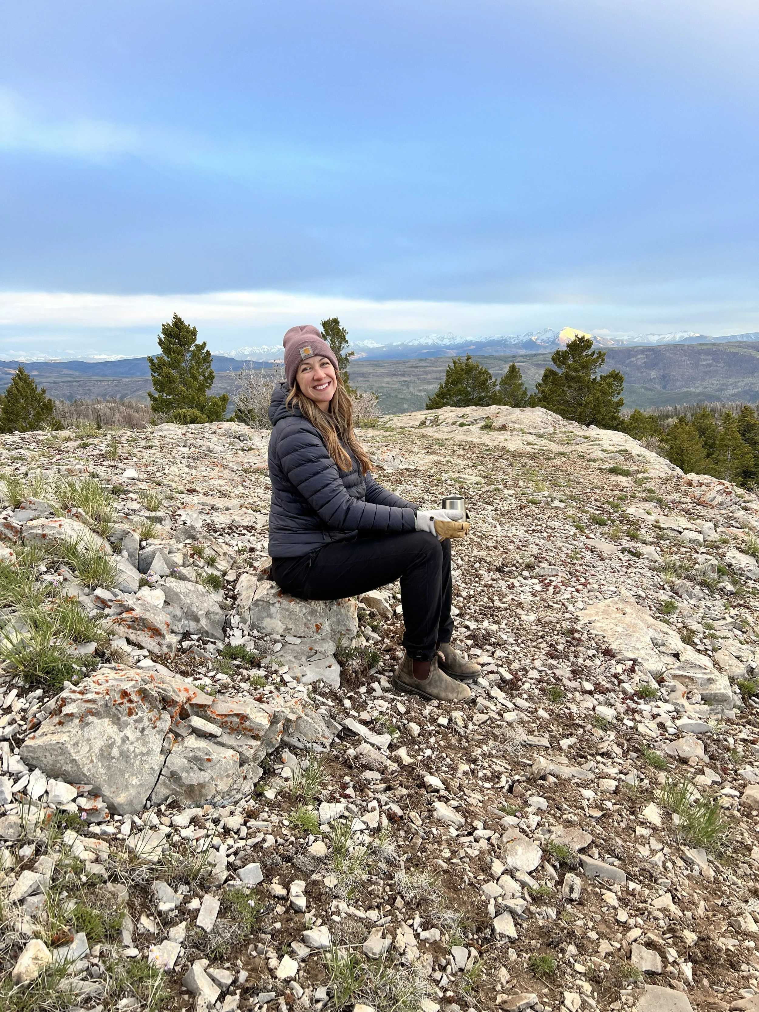 Stephanie Hands sitting among wildflowers with snow-capped Colorado mountains in the background.