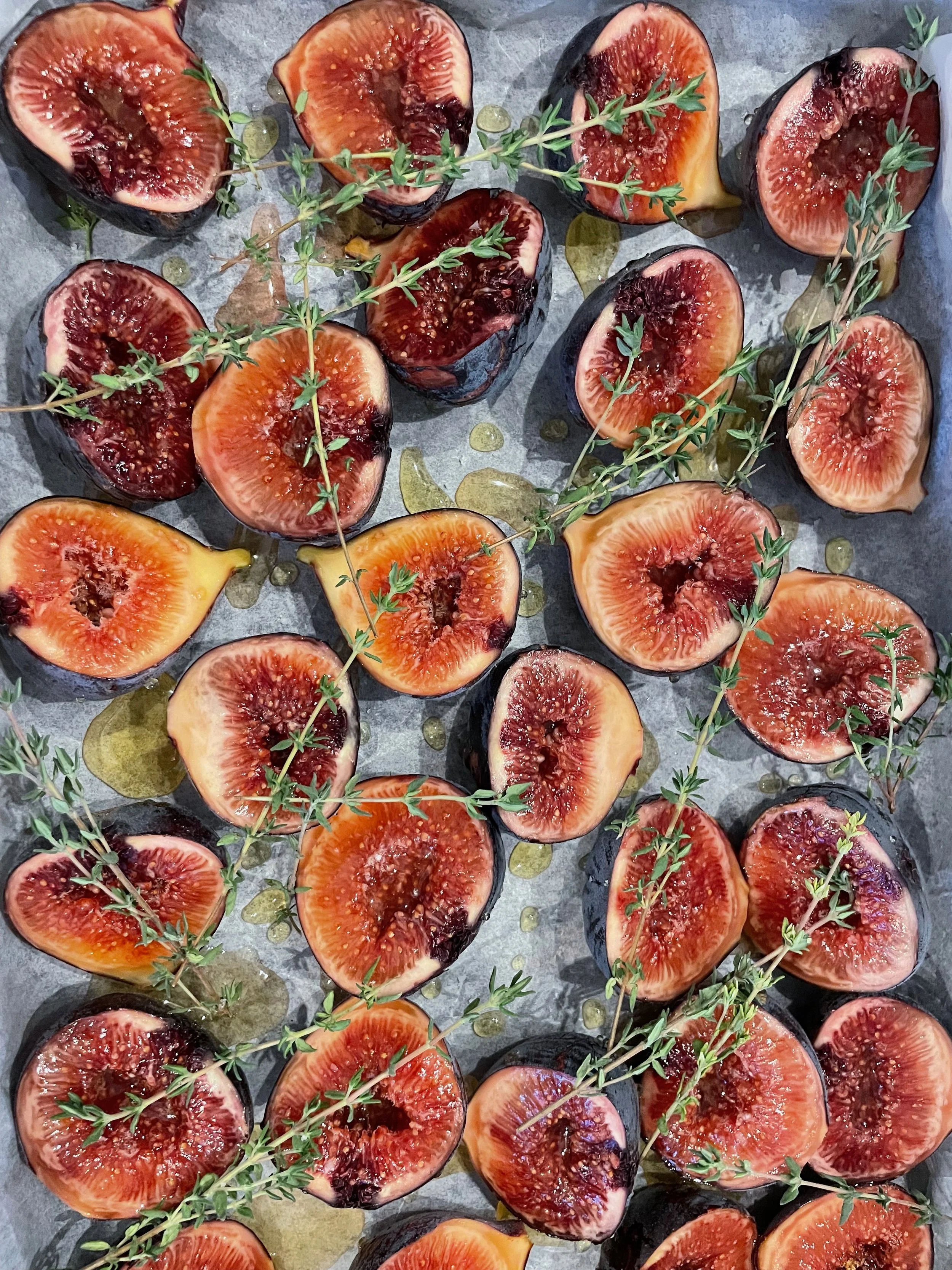 Halved figs with sprigs of thyme and olive oil drizzled on a baking sheet.