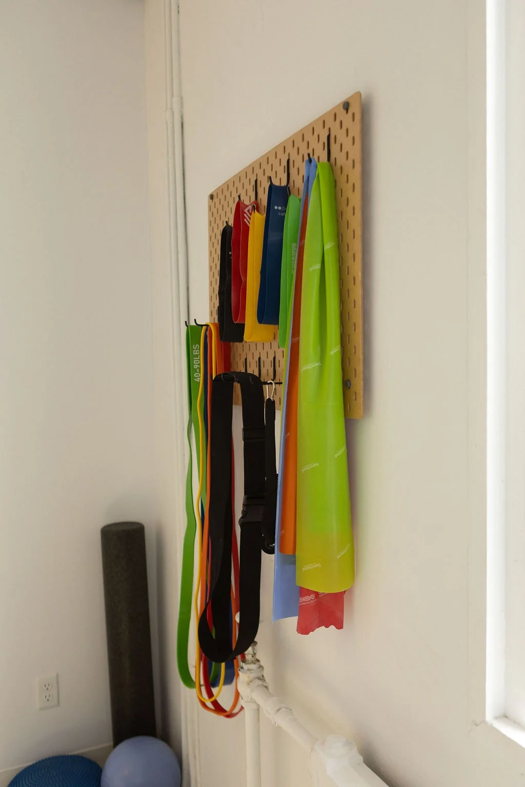 Pegboard with elastic and belts hanging on hooks in a room.