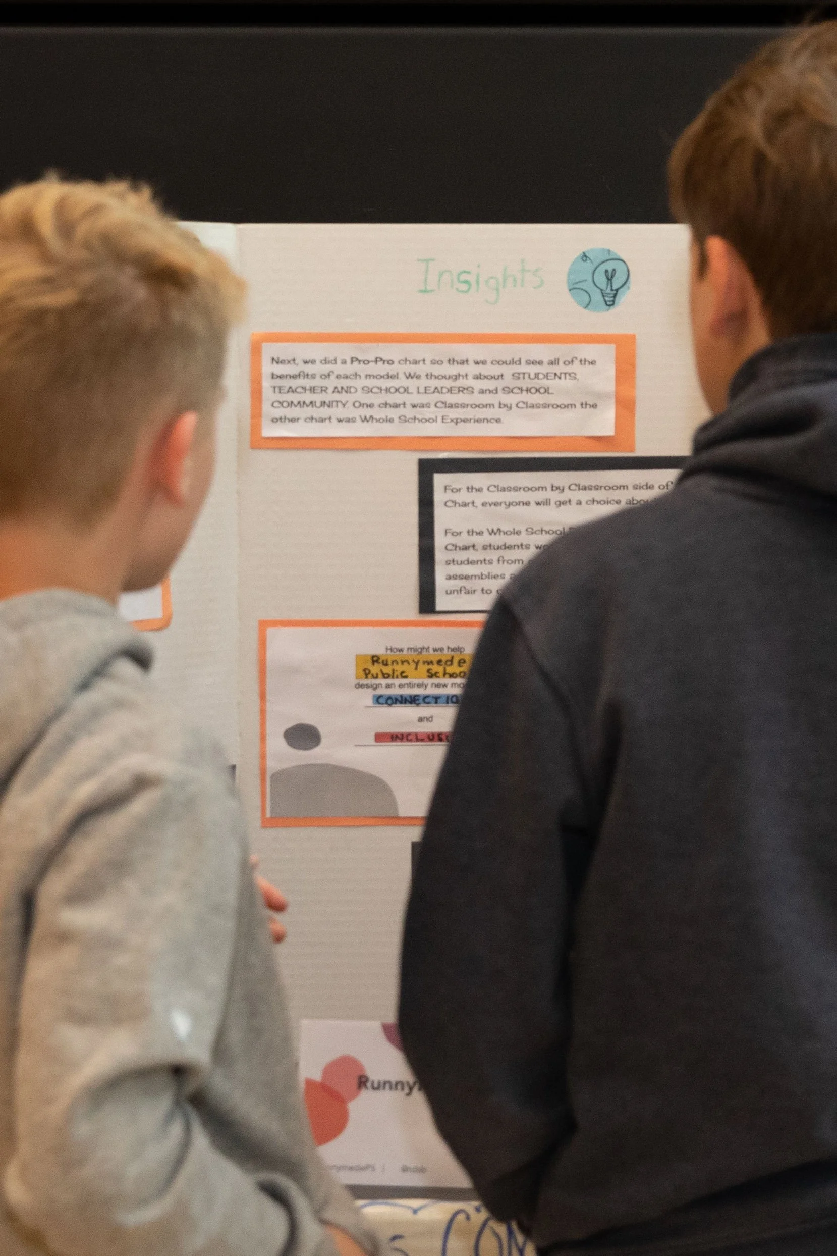 Two students standing in front of a classroom project display board discussing the content.