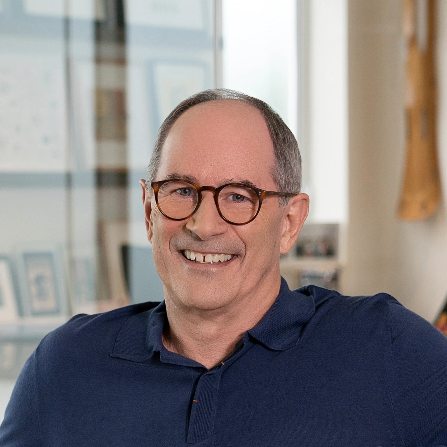 A middle-aged man with short hair and glasses smiling in a well-lit indoor setting.