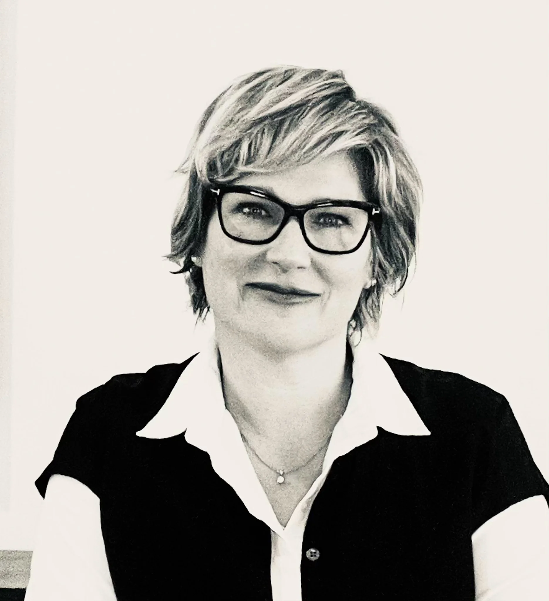 Black and white portrait of a woman with short hair, glasses, and a professional outfit, smiling slightly, against a plain background.