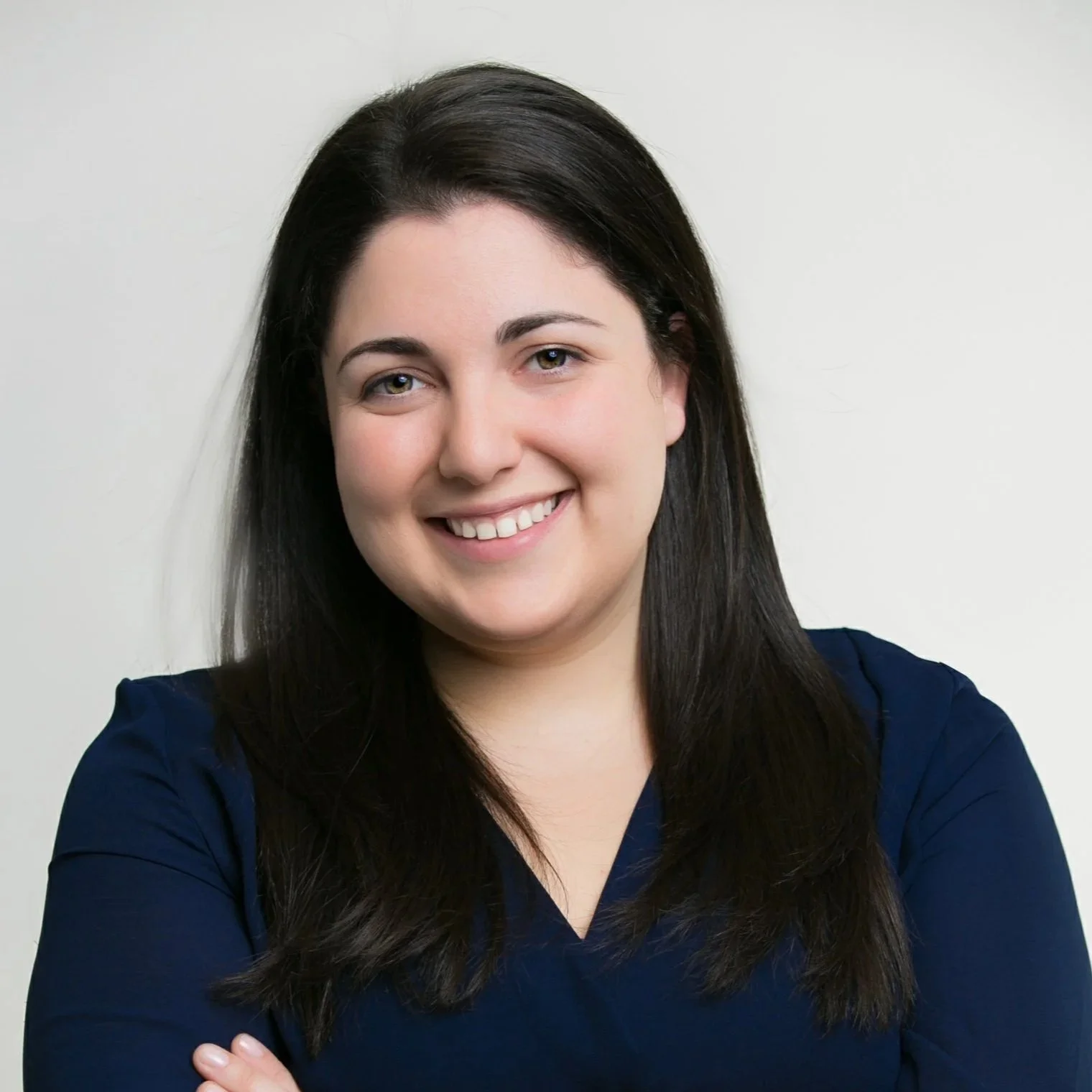 Portrait of a smiling woman with dark brown hair, wearing a navy blue top, against a plain background.