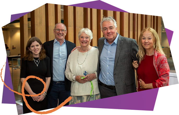 Group of five smiling people standing together indoors, with a wooden slat wall behind them.