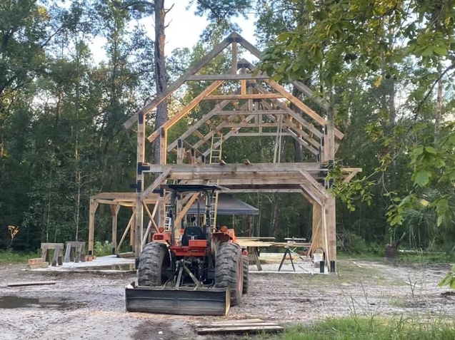 Wooden house under construction in a wooded area with a tractor in front.