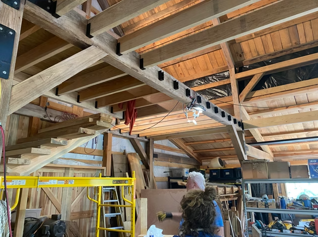 Construction workers working inside a wooden building under renovation with ladders and tools.