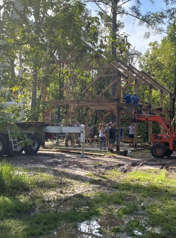 Construction workers building a wooden structure outdoors with trees in the background.