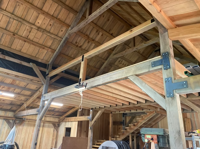 Interior of a wooden barn or workshop under construction, showing scaffolding and a ladder.