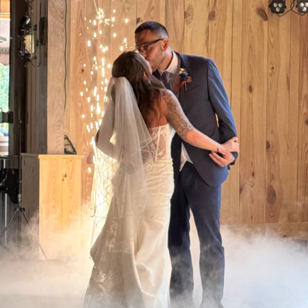 Bride and groom sharing a kiss during their wedding ceremony with sparks and fog effects in the background.