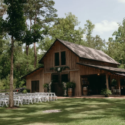 Outdoor rustic barn decorated for an event with white chairs arranged outside on a lawn.