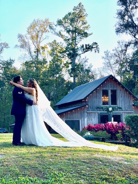Bride and groom dancing outdoors in front of a rustic barn at sunset.