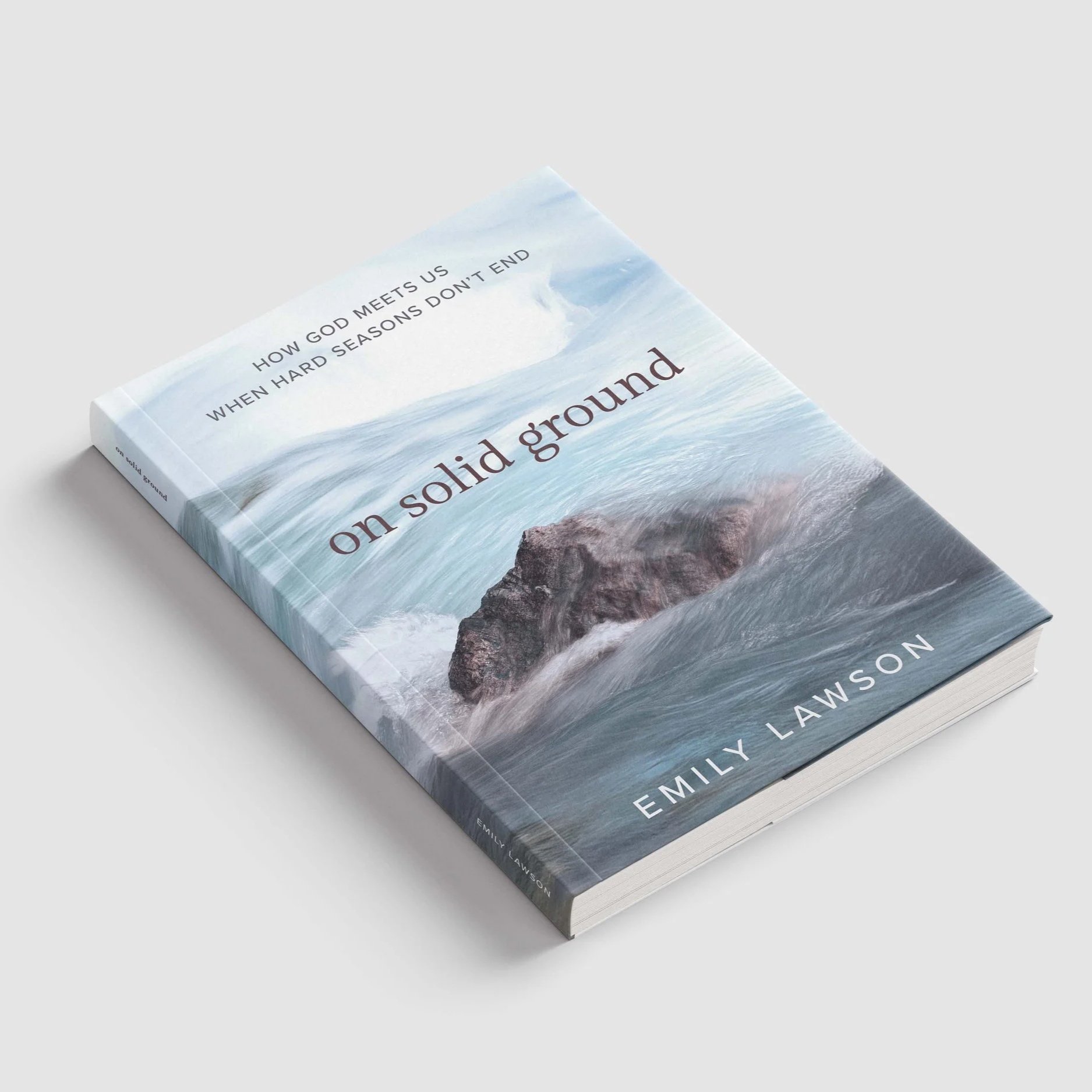 Close-up of a book titled 'On solid ground' with the subtitle 'How God meets us when hard seasons don’t end' by Emily Lawson, with an ocean scene on the cover