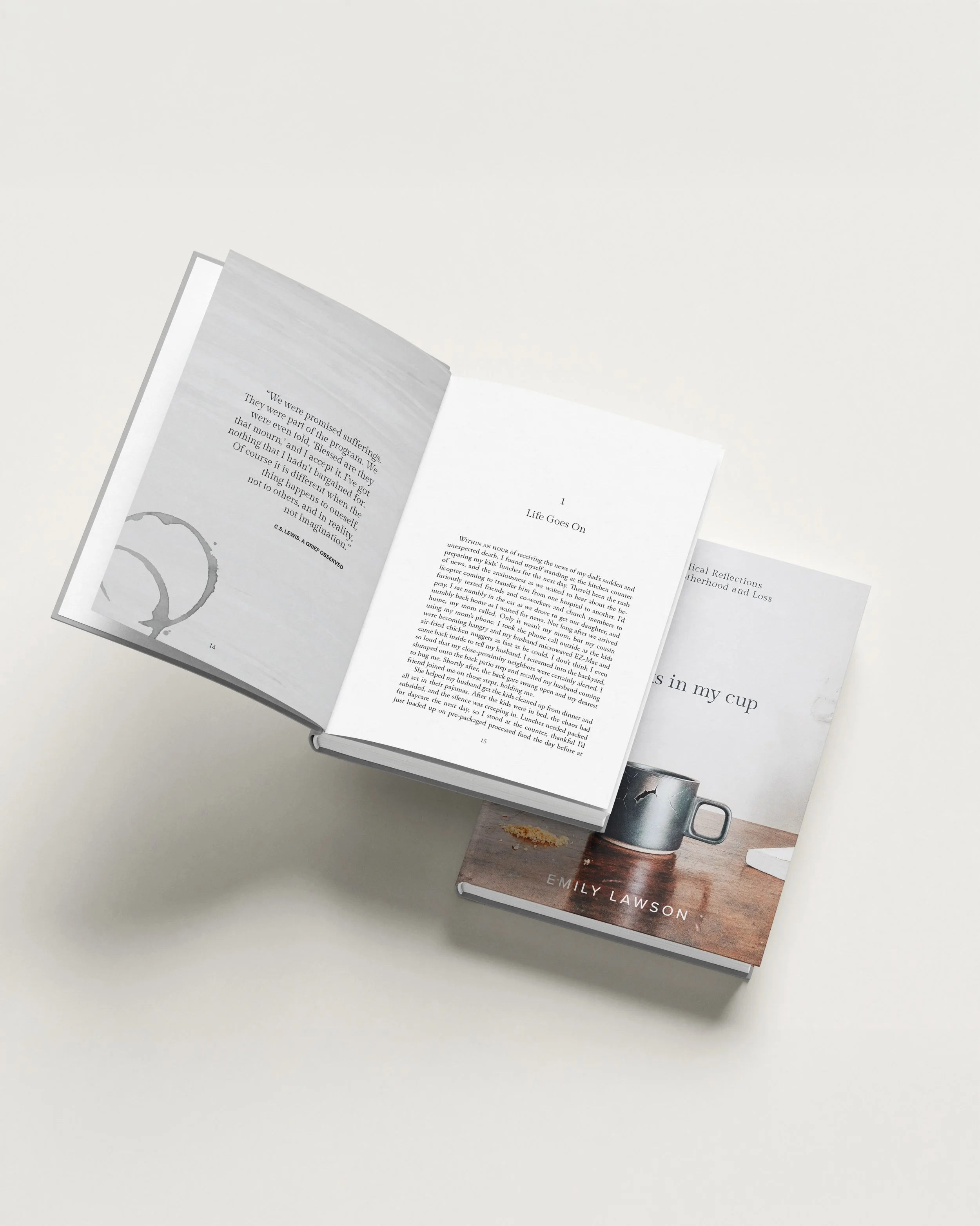 Open book with visible text and illustration, placed on top of another book with a visible cover featuring the author's name, Emily Lawson, and a picture of a coffee mug on a wooden table.
