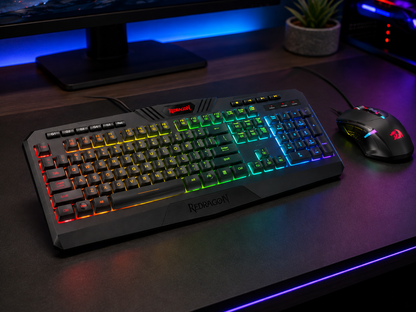 Redragon-style full-size RGB gaming keyboard and wired gaming mouse on a dark desk with colorful backlighting in a home PC setup.