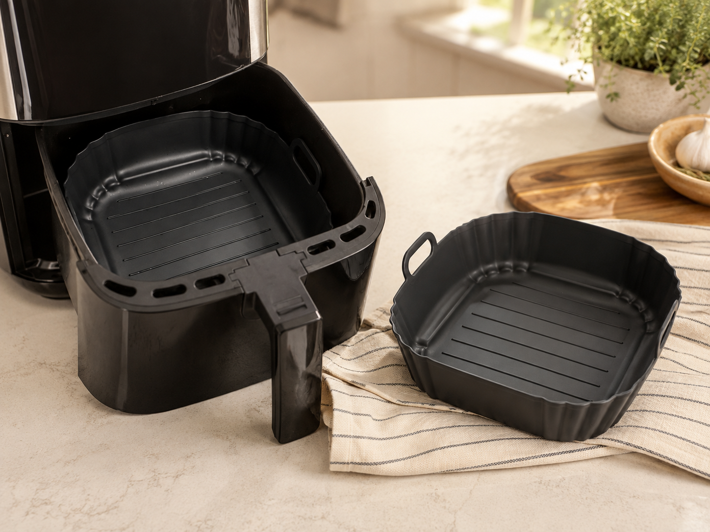 Black reusable air fryer trays displayed on a bright kitchen countertop beside a dual-basket air fryer.