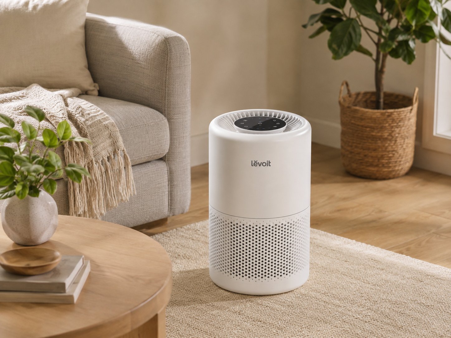 White Levoit air purifier placed beside a sofa in a warm, neutral living room with natural light and greenery.