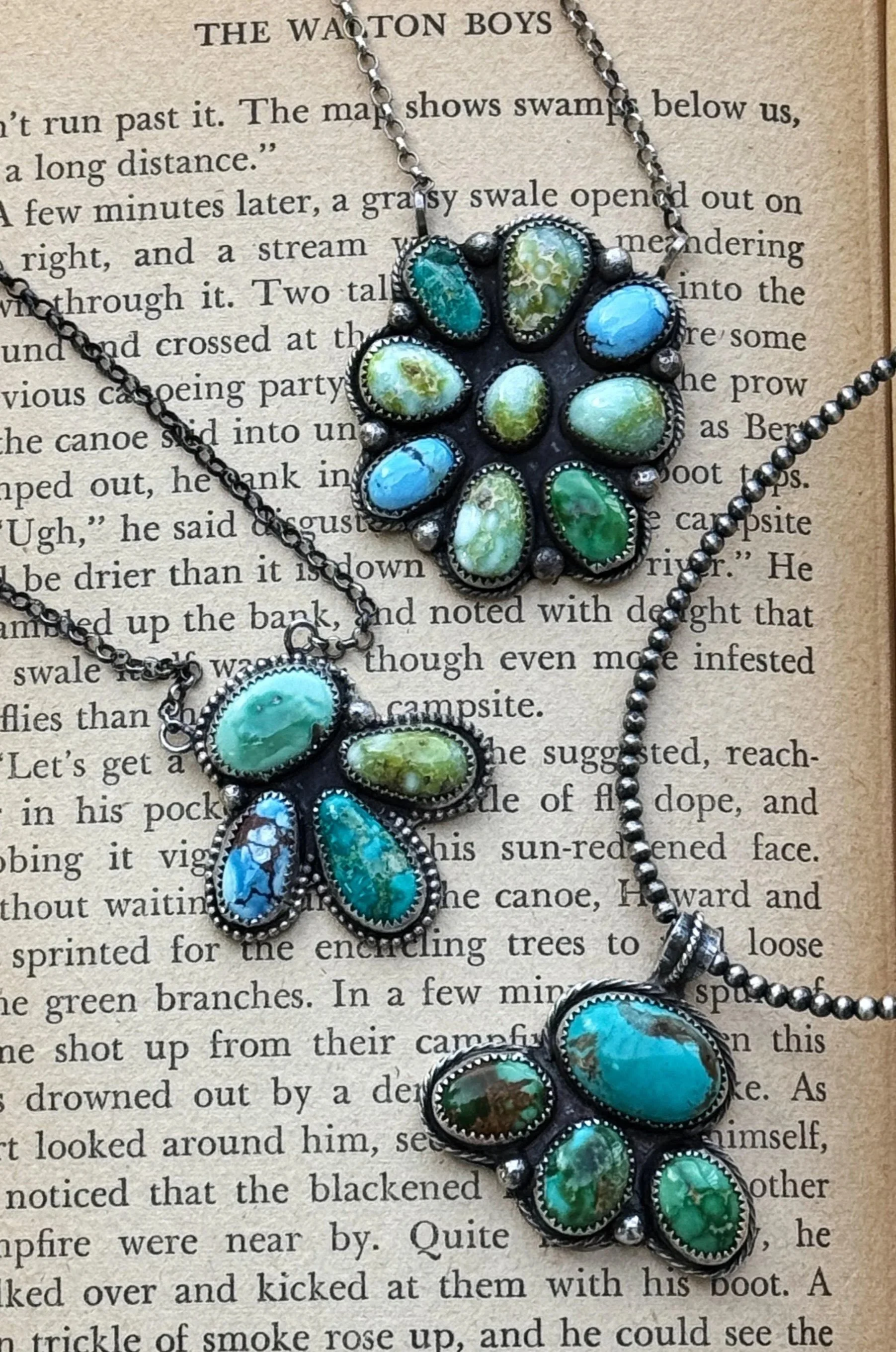 A vintage necklace with turquoise and green oval stones, set in silver, on a page of a book about the Watton Boys.