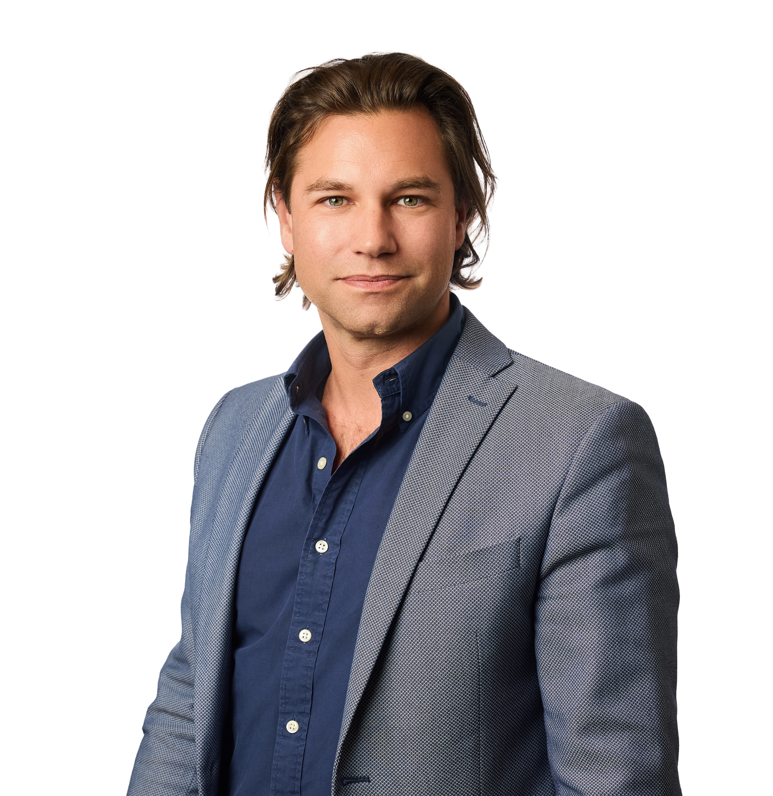 A close-up portrait of a man with green eyes and brown hair. He is wearing a gray blazer and a dark blue shirt, against a plain white background.