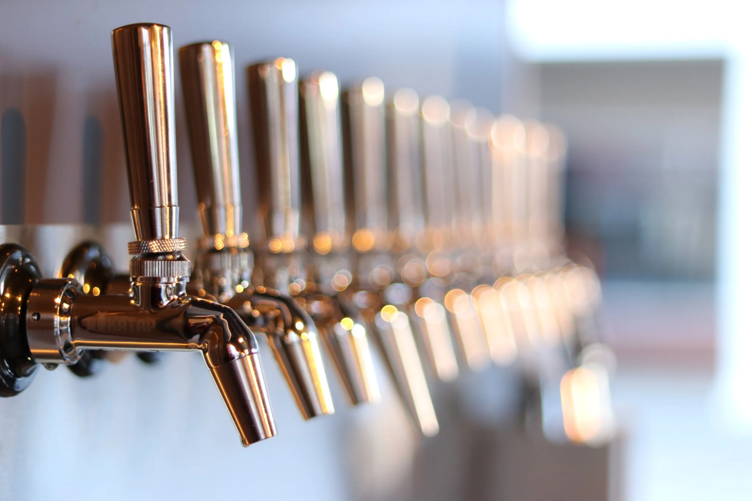 Close-up of a row of metallic beverage taps mounted on a wall, with a blurry background.