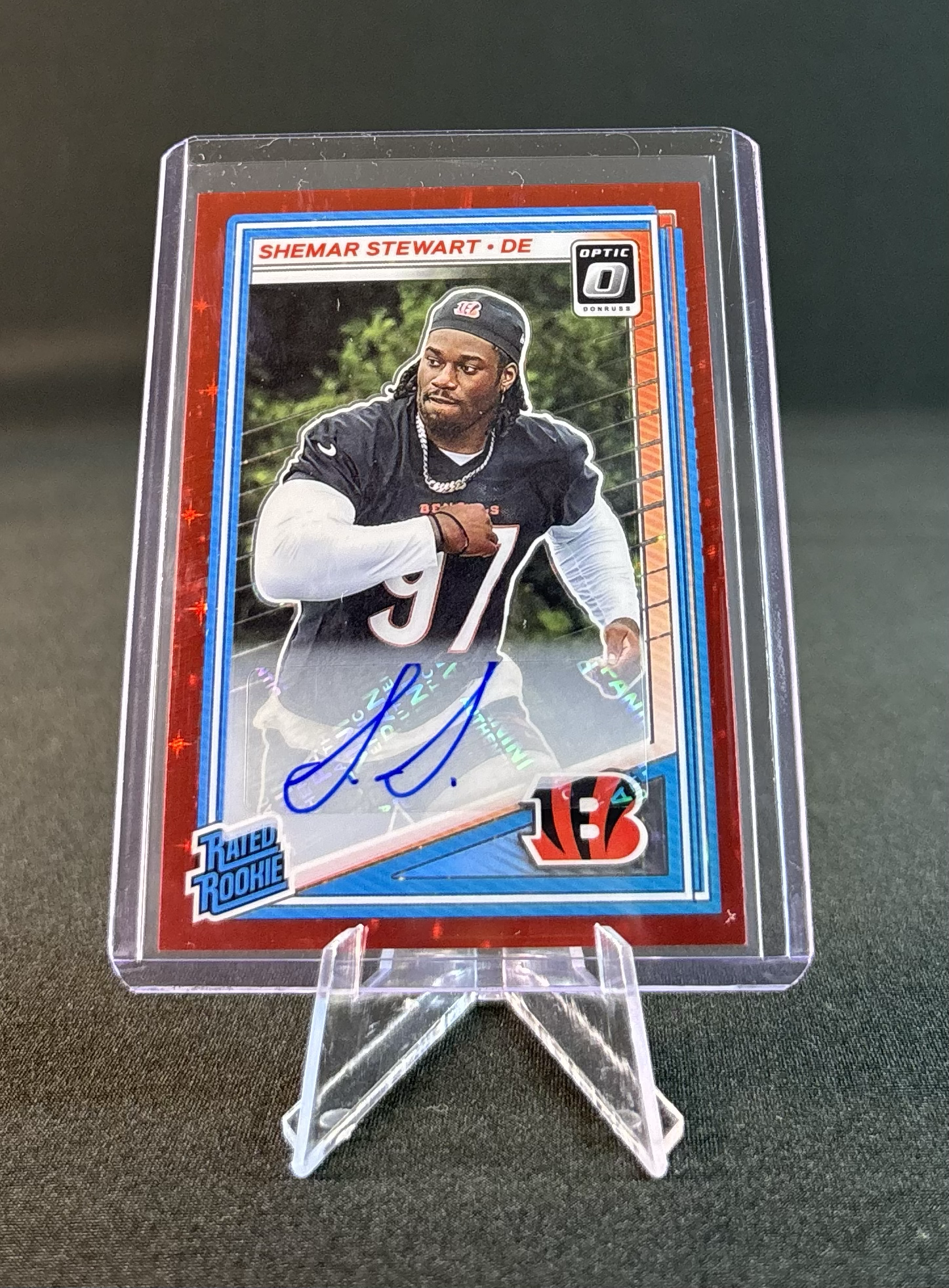 A collectible football trading card of Shemar Stewart, a rookie player for the Cincinnati Bengals, signed in blue ink, displayed in a clear plastic stand.