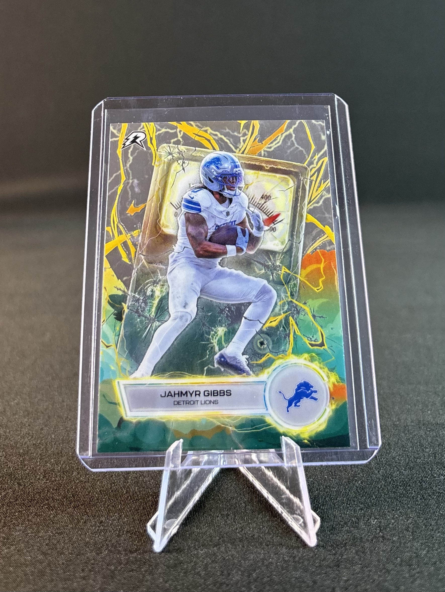 A collectible trading card of football player Jahmyr Gibbs from the Detroit Lions, encased in a clear plastic display with lightning and storm background art.