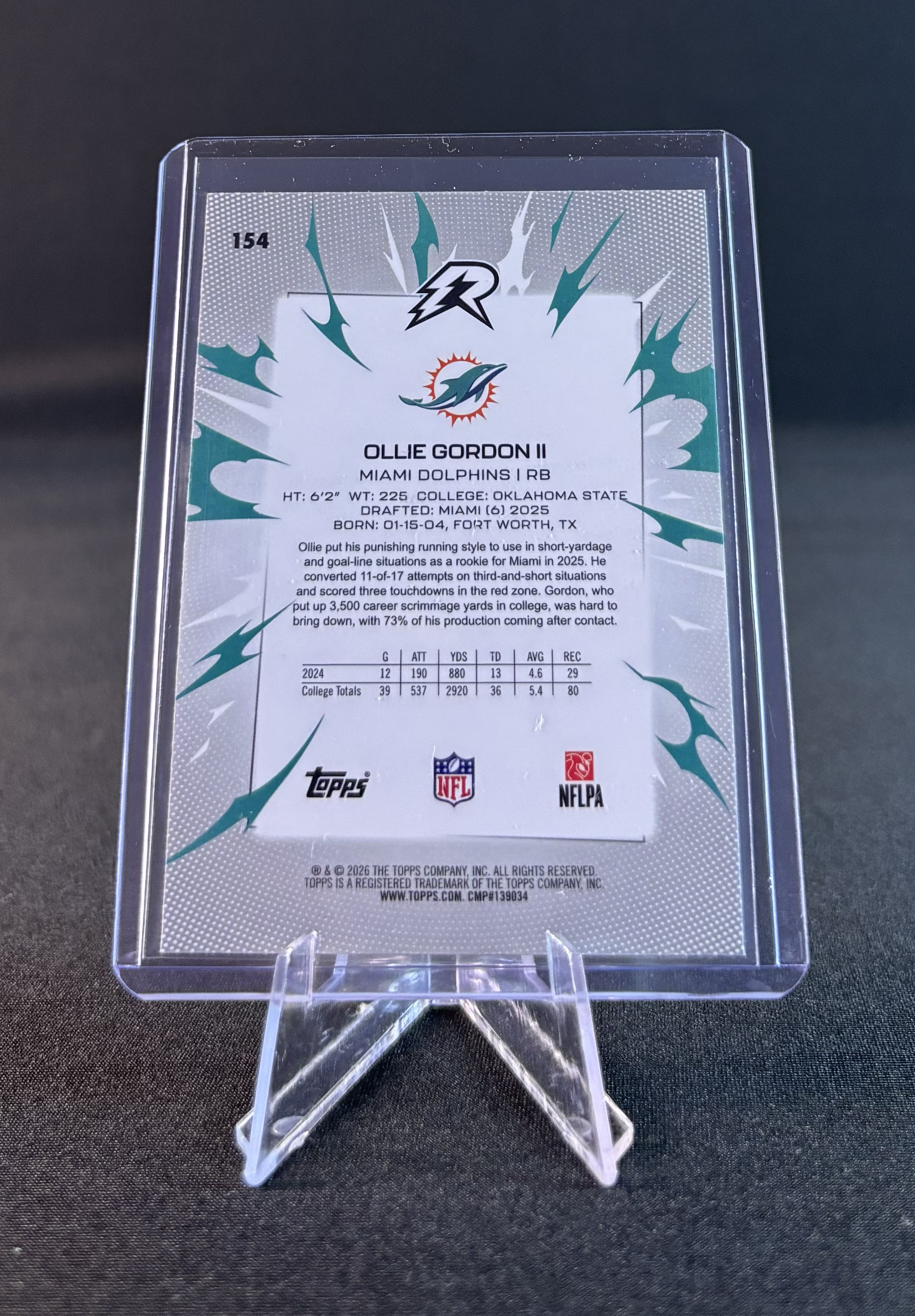 A collectible sports trading card encased in a clear plastic display stand. The card features a Miami Dolphins player profile with the name Ollie Gordon II, a running back, including stats and biographical information.