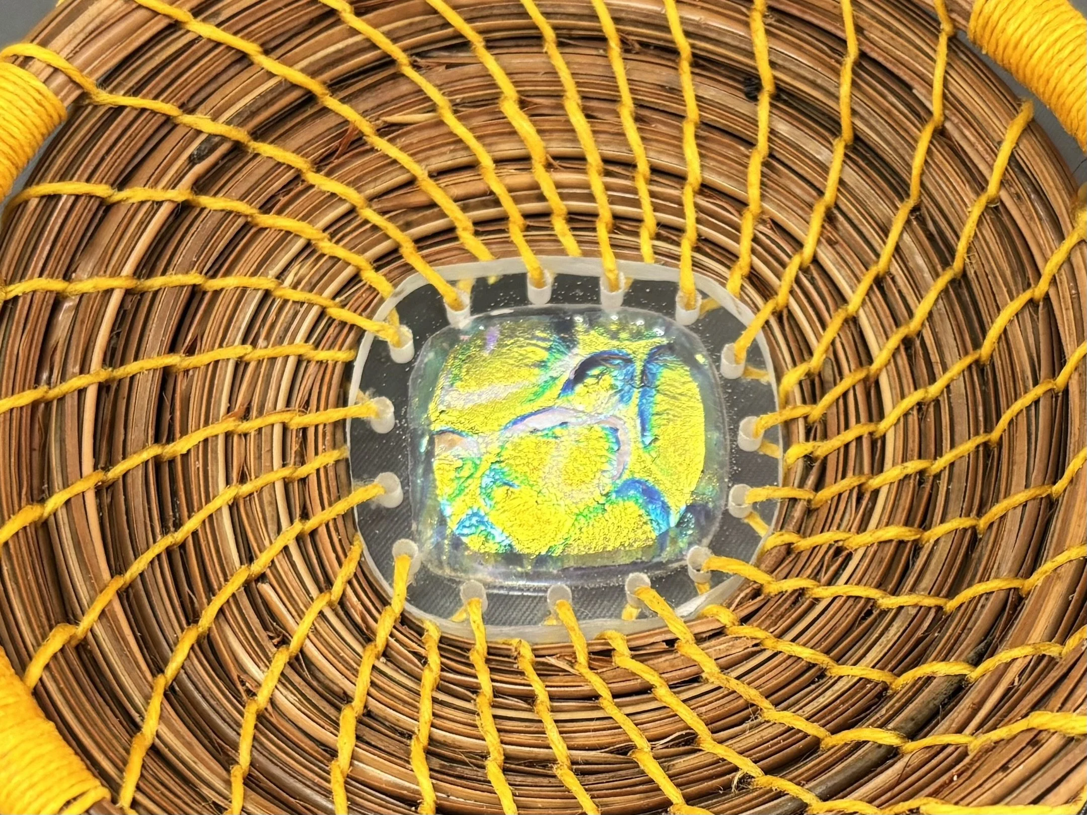 Close-up of the dichroic glass center of Held in Light, surrounded by radiating bright autumn yellow thread and natural pine needle coils.