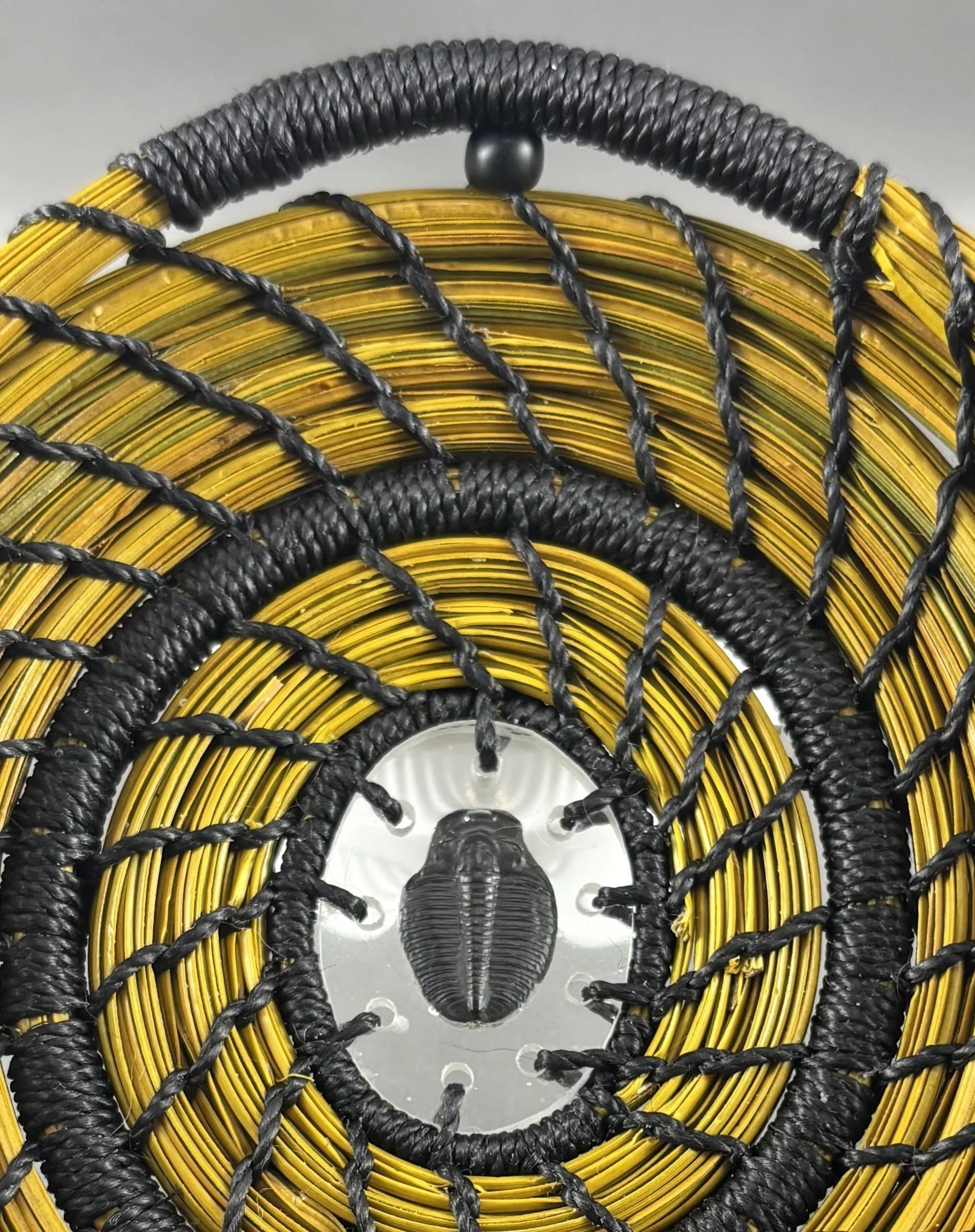 Detail view of Primeval Gold showing antique-gold dyed pine needles, black spiral stitching, and black-wrapped rows